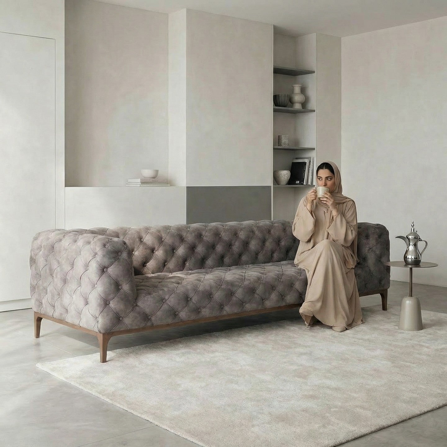 Woman sitting on a gray classic Chesterfield style sofa in a modern living room, holding a coffe cup
